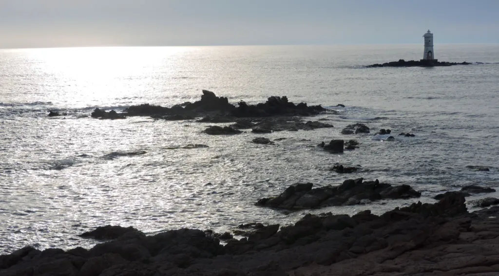 Scogli affioranti e fanale di Mangiabarche osservati dalla costa